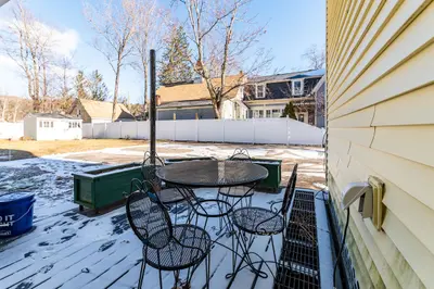 A snowy deck with a table and chairs, surrounded by houses in the background.