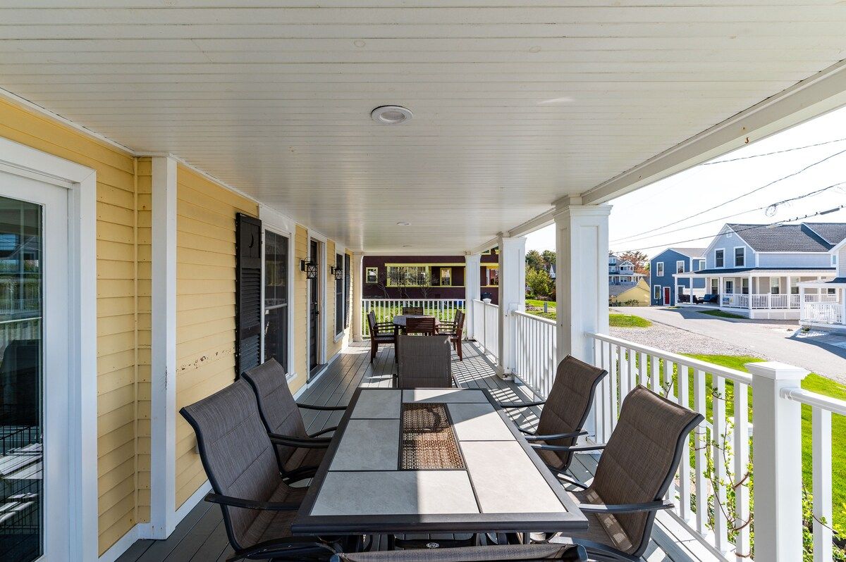 A spacious covered porch with a long table and chairs, perfect for outdoor dining or relaxation.