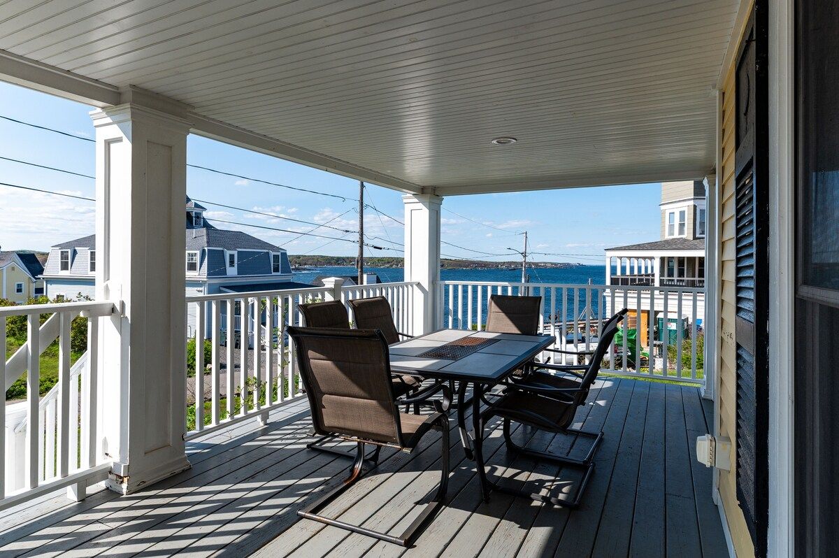 A spacious covered porch with a table and chairs overlooking the water.