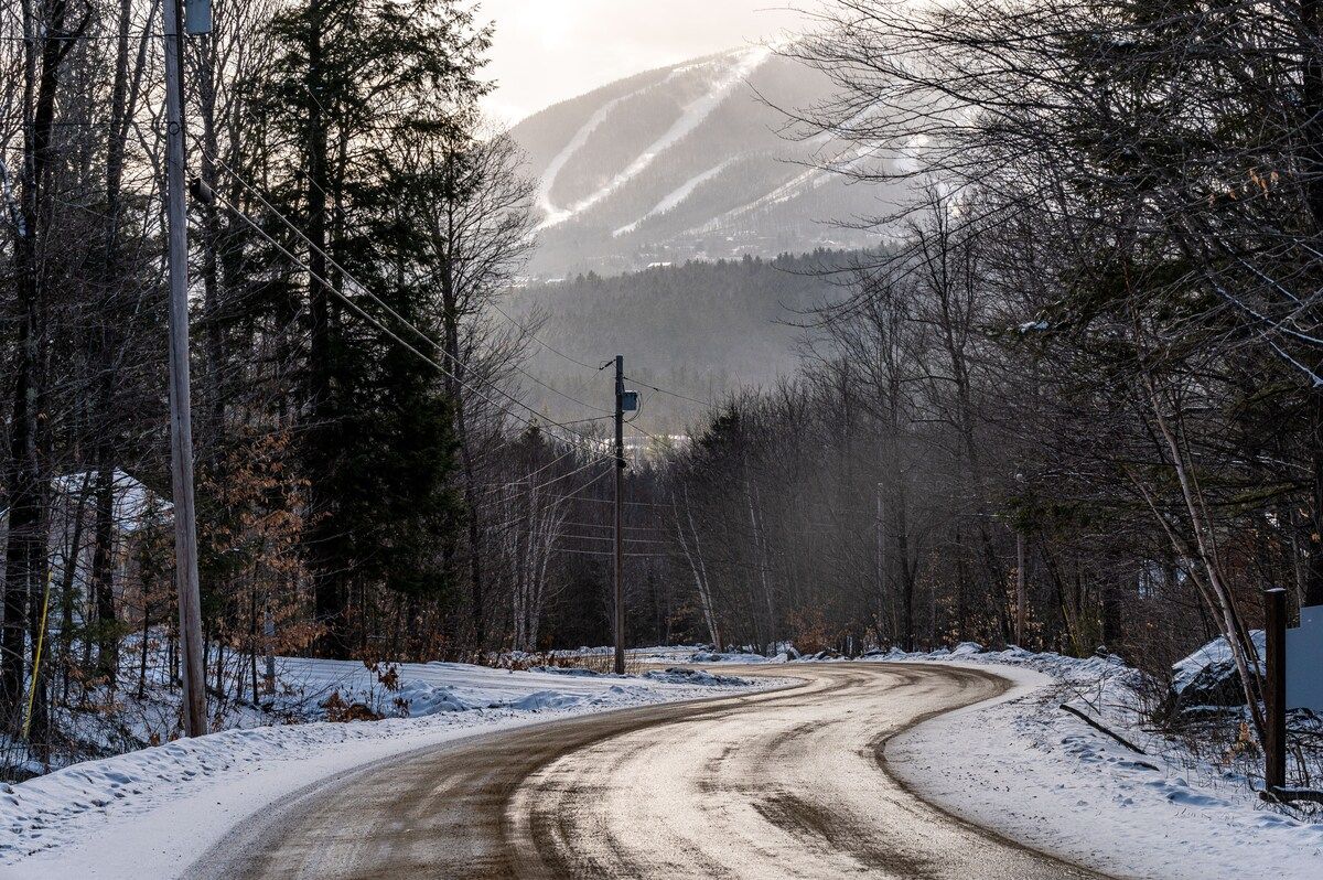 Snowy road leading to a mountain with ski trails in the distance.