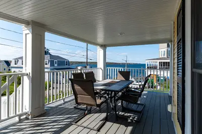 A spacious covered porch with a table and chairs overlooking the water.
