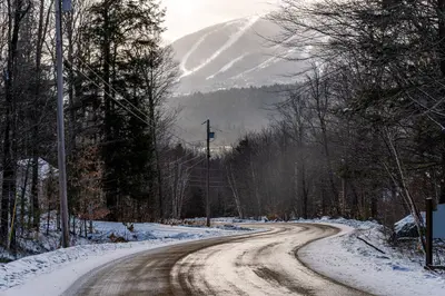 Snowy road leading to a mountain with ski trails in the distance.
