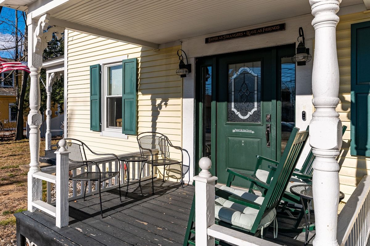 A cozy porch with green rocking chairs and a sign that says 'Enter as strangers, leave as friends'.