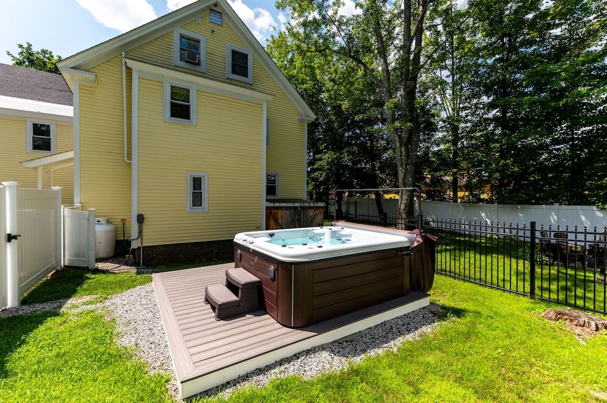 A backyard with a hot tub on a wooden deck surrounded by grass and trees.
