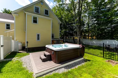 A backyard with a hot tub on a wooden deck surrounded by grass and trees.