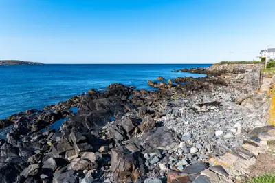 A rocky coastline with a house in the distance and a clear blue sky.