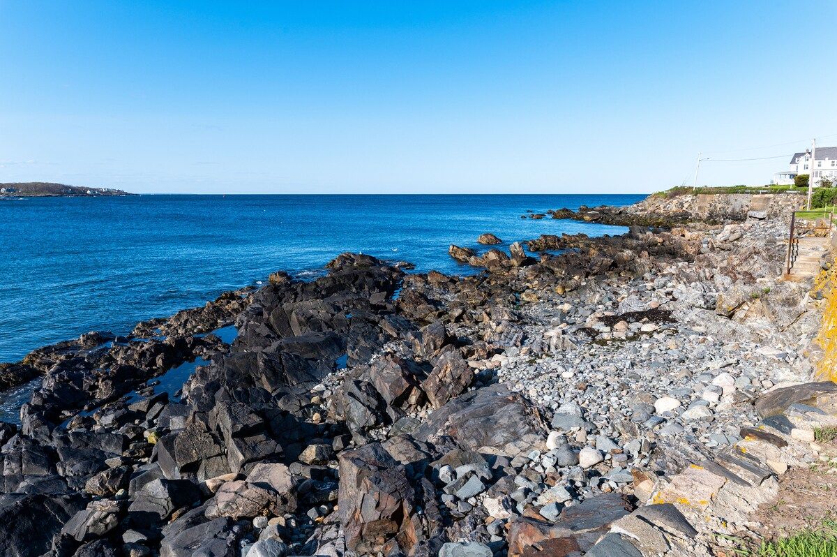 A rocky coastline with a house in the distance and a clear blue sky.