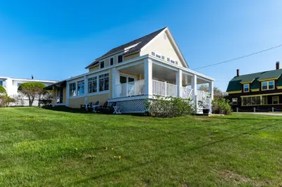 Large front porch with a white railing and a green roof