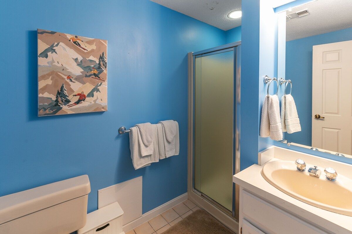 A bathroom with a white sink and mirror, featuring a painting of skiers on the wall.