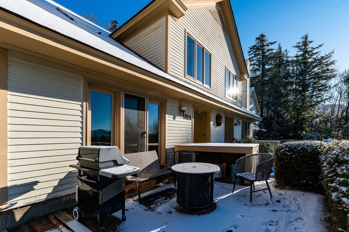 Snowy patio with a grill and outdoor furniture in front of a house